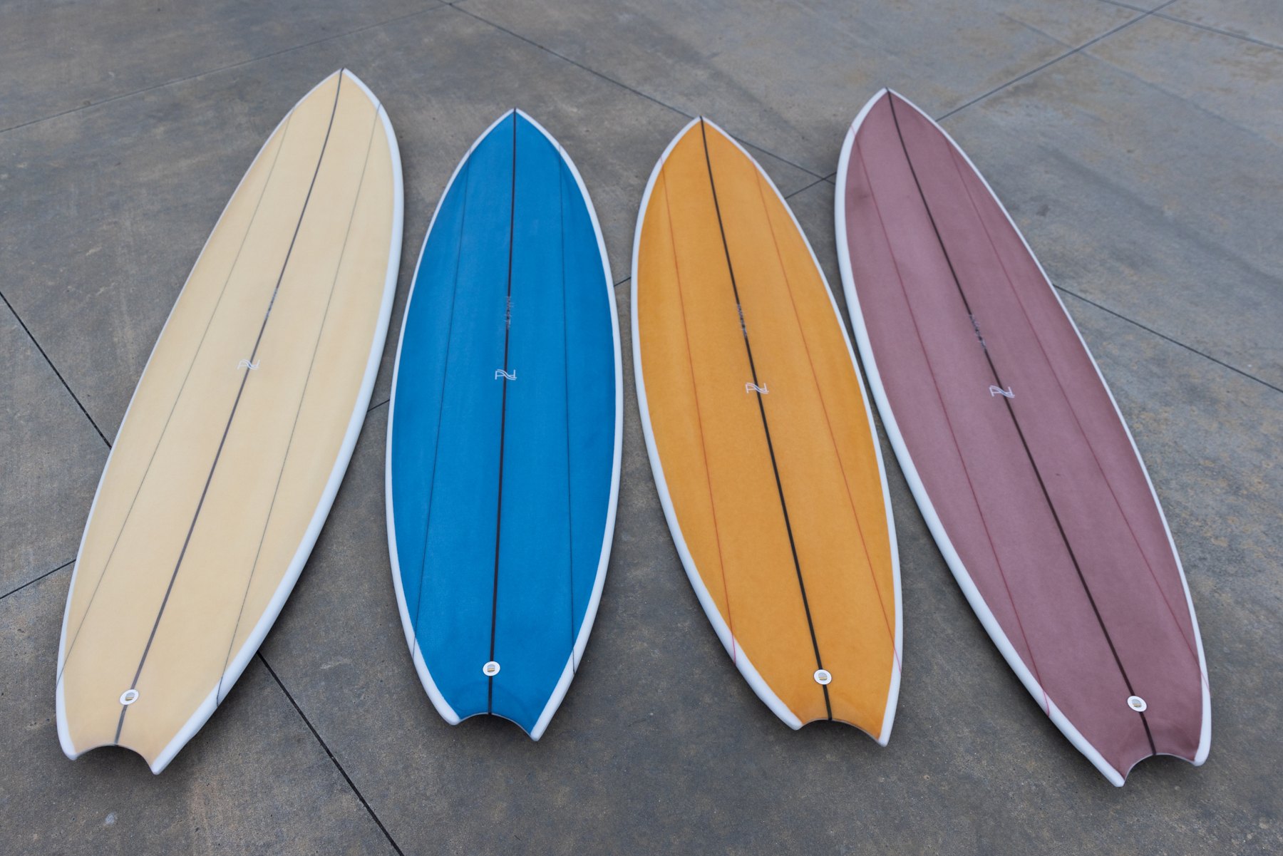 Four A&H Vessels Ordainer surfboards in cream, blue, amber and purple